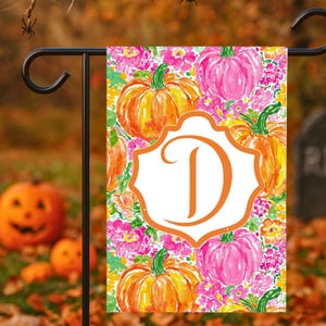 May include: A rectangular garden flag featuring a watercolor pattern of orange and pink pumpkins surrounded by pink and yellow flowers. In the center, a white scalloped frame with an orange border contains a large, bold, orange letter D.
