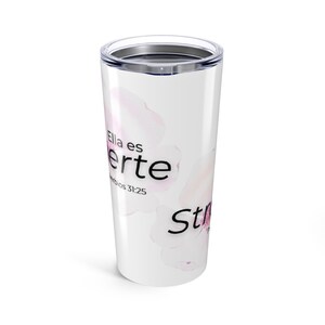 Puede incluir: Vaso de viaje blanco con tapa plateada. El vaso presenta un diseño floral en tonos rosas y las palabras "Ella es Fuerte" y "Strong" en texto negro. También es visible el texto "Proverbios 31:25".