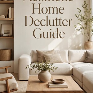May include: A digital graphic featuring the text Aesthetic Home Declutter Guide in dark brown serif font over a beige wall. The scene includes a white sofa, a wooden coffee table with a ceramic vase and bowl, and built-in shelves with decor.