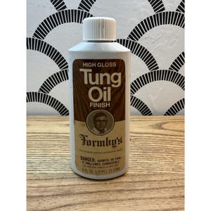 May include: A white bottle of Formby's Tung Oil Finish with a brown label. The label reads "HIGH GLOSS Tung Oil FINISH" and includes a portrait. The bottle contains 8 fl oz (1/2 pt).