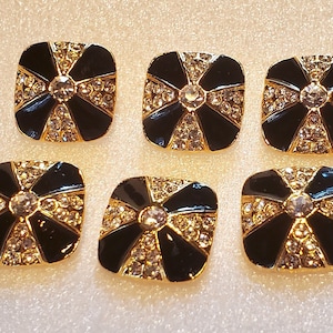 May include: Six black and gold square buttons with clear rhinestone accents. Each button has a cross-shaped design.