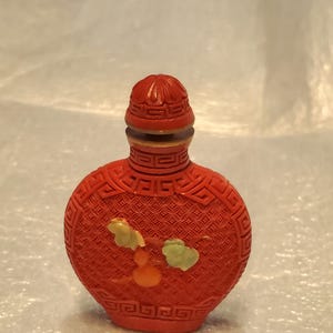 May include: A red Chinese snuff bottle with a carved design and a green and orange floral motif.