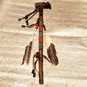 May include: A handcrafted Native American ceremonial pipe. The pipe features a wooden stem with leather wrappings, decorative beads in red, green, and white, and is adorned with feathers and leather fringe. The pipe is approximately 20 inches in length.