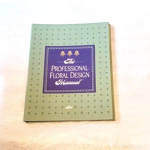 May include: A green book titled "The Professional Floral Design Manual." The cover features a dark blue rectangle with gold floral accents and white text. The book has a dotted pattern and the letters "afs" at the bottom.