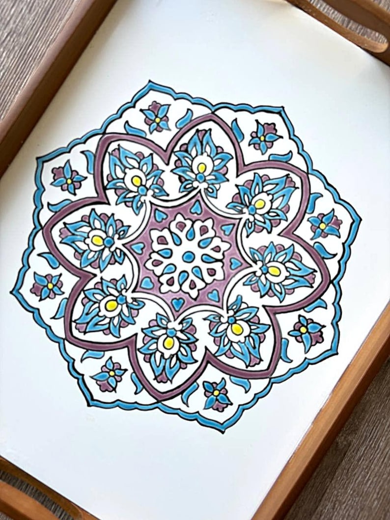May include: A decorative tray with a white surface and a detailed floral mandala design. The mandala features blue, purple, and yellow accents, framed by a wooden border. The floral pattern is symmetrical and intricate.