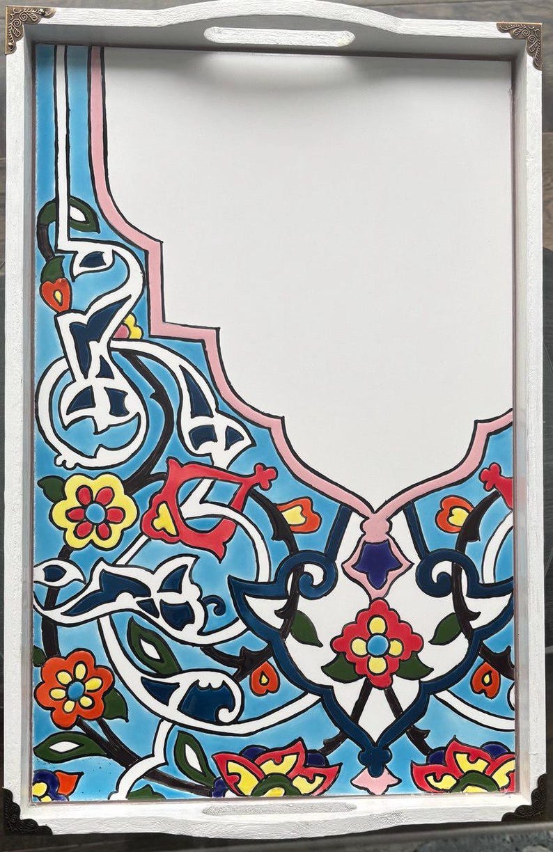 May include: White wooden serving tray with a colorful, ornate tile design. The tile features a blue background with floral and arabesque patterns in red, yellow, and white. The tray has a handle and decorative metal corners.