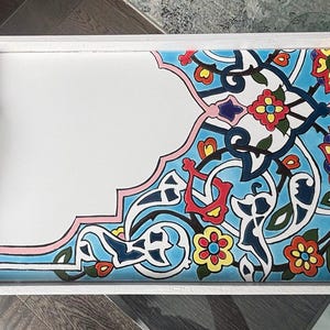 May include: White serving tray with a decorative corner featuring a blue, red, yellow, and pink floral design. The tray has white handles and gold corner accents.