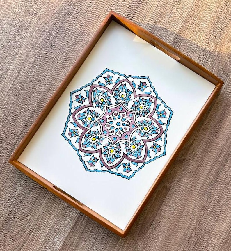 May include: A rectangular wooden serving tray with a white interior featuring a detailed floral design in shades of blue, purple, and yellow. The tray has a brown wooden frame and integrated handles, suitable for serving food or displaying decorative items.