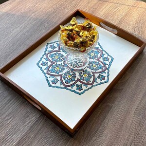 May include: A rectangular wooden serving tray with a white interior featuring a blue, teal, and maroon floral design. A glass bowl filled with wrapped candies sits in the center. The tray has built-in handles.