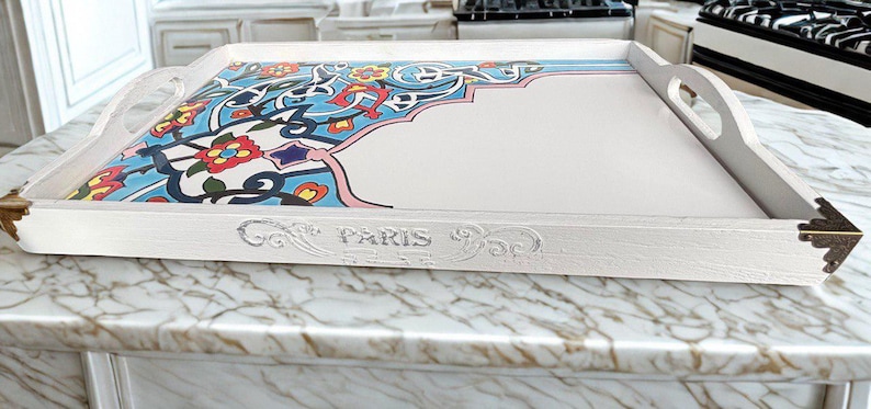 May include: A rectangular white serving tray with handles and decorative corner accents. The tray features a colorful floral and geometric design in blue, red, and yellow. The word "PARIS" is embossed on the side.