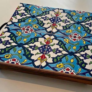 May include: Decorative serving tray with a floral tile design. The tray features a wooden base and metal handles. The tiles have a blue background with white, red, yellow, and green floral patterns. The tray measures approximately 12 inches long and 8 inches wide.