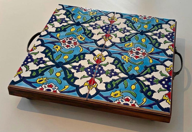 May include: Decorative serving tray with a floral tile design. The tray features a wooden base and metal handles. The tiles have a blue background with white, red, yellow, and green floral patterns. The tray measures approximately 12 inches long and 8 inches wide.