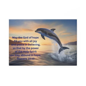 May include: A canvas print featuring a dolphin leaping out of the ocean. The image has a vibrant sunset backdrop with text that reads "May the God of hope fill you with all joy and peace in believing...Romans 15:13."