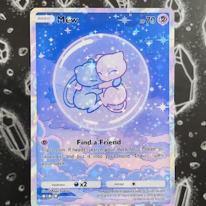 Könnte beinhalten: Holografische Pokémon-Sammelkarte mit zwei Mew-Charakteren in einer Blase. Die Karte hat ein blau-violettes Farbschema mit Sternen- und Wolkenakzenten. Der Text enthält "Mew", "HP 70" und "Find a Friend".