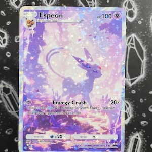Op de afbeelding: Een holografische Espeon Pokémon-kaart met paarse en witte tinten. De kaart toont de naam "Espeon" en de aanval "Energy Crush", samen met andere spelgegevens. De illustratie toont een gestileerde Espeon in een bosrijke omgeving.