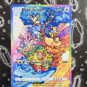 Op de afbeelding: Een holografische Pokémon-verzamelkaart met een illustratie van Eevee-evoluties in een kleurrijke scène. De kaart toont de tekst "Eeveelution", "Elemental Strike" en "HP 320". De illustratie toont een levendig landschap met meerdere Pokémon-personages.