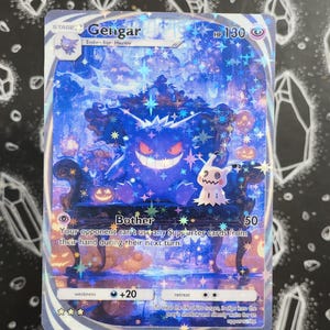 Könnte beinhalten: Eine holografische Gengar Pokémon-Sammelkarte. Die Karte zeigt einen lila Gengar-Charakter auf einem Thron, mit einem Mimikyu-Charakter. Die Karte trägt den Text "Bother" und "Your opponent can't use any Supporter cards from their hand during their next turn."