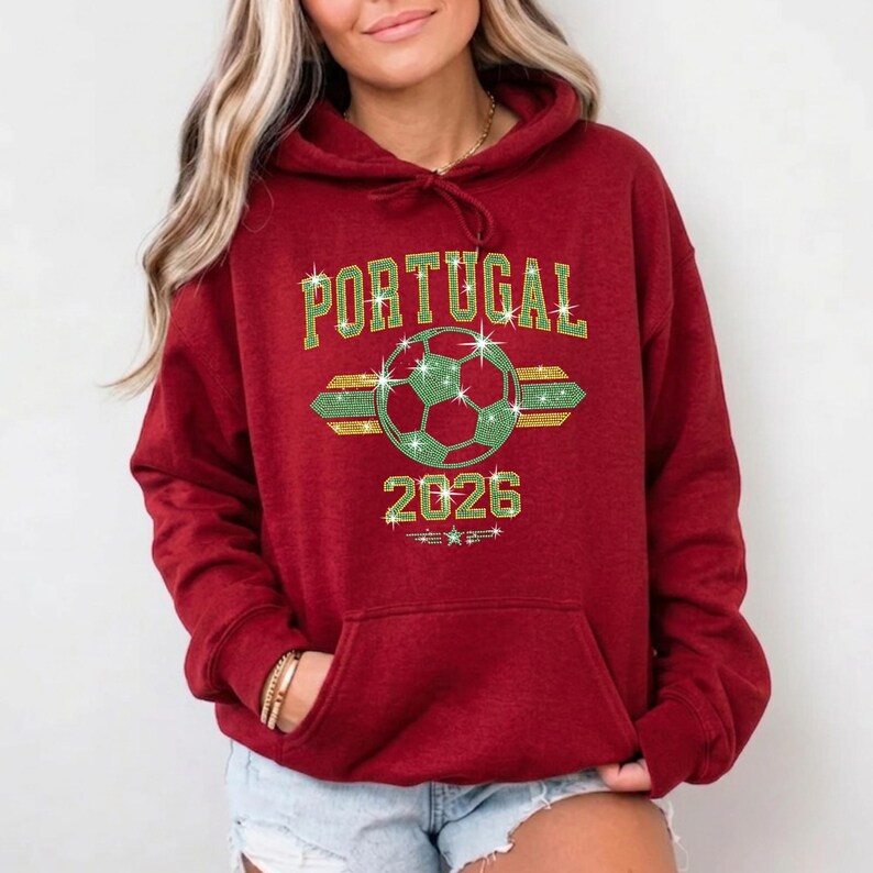 May include: Red hoodie featuring the customized Portugal rhinestone soccer graphic. The high-shine stones bring a trendy, athletic vibe to the classic hooded garment with a front pouch pocket.