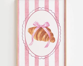 May include: Watercolor print of a croissant tied with a pink ribbon, set within a pink scalloped oval. The background features vertical pink and white stripes, all framed in a light wood frame. A charming bakery-themed artwork.