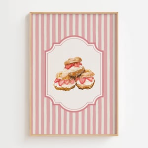 Pode incluir: Uma impressão emoldurada com uma ilustração em aquarela de três profiteroles de morango. A imagem é definida contra um fundo listrado rosa e branco, emoldurado em madeira clara. A impressão tem uma borda decorativa.