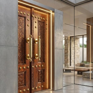 May include: A pair of intricately carved wooden doors with brass hardware and decorative studs. The doors are framed by concrete walls and illuminated by vertical LED lights, creating a warm, inviting entrance.