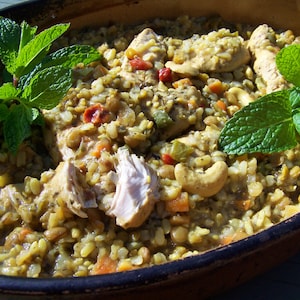 May include: A close-up of a bowl of chicken and rice with fresh mint leaves on top. The dish is made with lentils, cashews, and other vegetables.