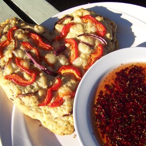 May include: A heart-shaped flatbread topped with red peppers, onions, and cheese, served with a bowl of red sauce.
