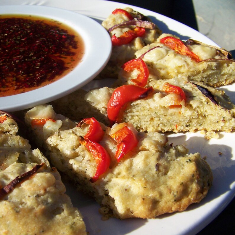 May include: A white plate with a bowl of red sauce and several pieces of focaccia bread topped with red peppers and cheese.