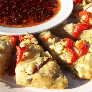 May include: A white plate with several slices of focaccia bread topped with red peppers and cheese. A small white bowl with a red sauce is in the background.