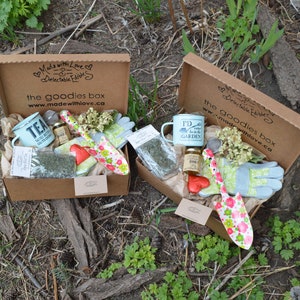 Puede incluir: Dos cajas de regalo abiertas con art&iacute;culos de jardiner&iacute;a. Cada caja contiene una taza, guantes, una paleta y otros objetos peque&ntilde;os. Las cajas est&aacute;n sobre papel marr&oacute;n, con el texto "the goodies box" y "Made with Love" en la caja.