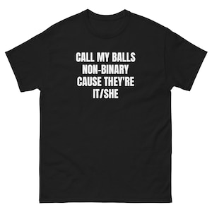 May include: A black short-sleeved t-shirt featuring white text printed on the chest that reads: CALL MY BALLS NON-BINARY CAUSE THEY'RE IT/SHE. The garment has a crew neckline and a standard fit, constructed from a solid black fabric throughout.