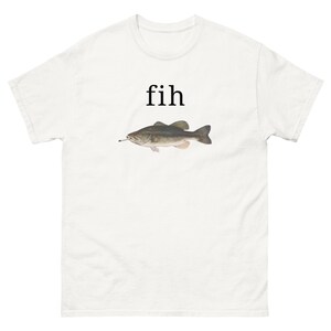 Op de afbeelding: Een wit T-shirt met korte mouwen en een afbeelding van een grijze vis met een sigaret in de mond. Boven de vis staat het woord fih gedrukt in een eenvoudig zwart schreeflettertype. Het ontwerp is gecentreerd op de borst van het shirt.