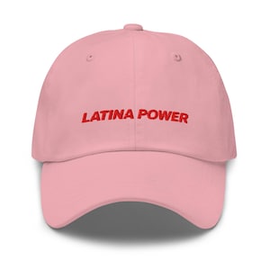 Op de afbeelding: Een lichtroze honkbalpet met de tekst LATINA POWER in rood borduursel op de voorzijde. De pet heeft een gestructureerde kroon, een gebogen klep en een knoop aan de bovenkant, wat zorgt voor een strak en eenvoudig ontwerp.