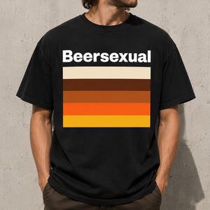 Peut inclure: Un t-shirt noir à manches courtes avec le texte blanc Beersexual au-dessus d'un graphique rectangulaire composé de cinq bandes horizontales dans des tons crème, brun foncé, brun moyen, orange et jaune, disposées en pile.