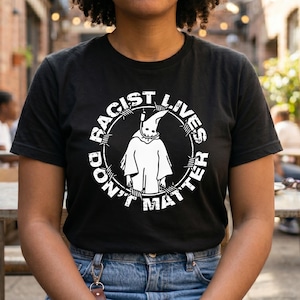 May include: A black short-sleeved t-shirt featuring a white circular graphic. The design depicts a hooded figure in the centre, surrounded by barbed wire, with the text "RACIST LIVES DON'T MATTER" printed in a distressed font around the circle.