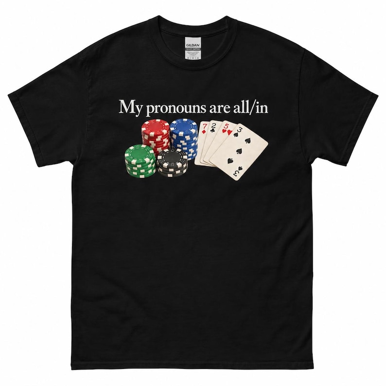 May include: A black short-sleeve t-shirt featuring a graphic of four stacks of colorful poker chips and a hand of playing cards. Above the graphic, the white text reads, My pronouns are all/in. The shirt has a standard crew neckline and short sleeves.