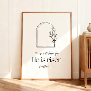 May include: A framed print with a minimalist design. The artwork features a black line drawing of an arch and a sprig of leaves. The text reads "He is not here for He is risen Matthew 21:6" in a modern font. The frame is brown.