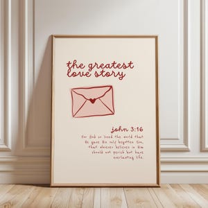 Może przedstawiać: Oprawiony wydruk artystyczny z napisem "the greatest love story" w czerwonym skrypcie. Poniżej znajduje się różowa ilustracja koperty z sercem. Tekst "john 3:16" i werset biblijny znajdują się na dole.