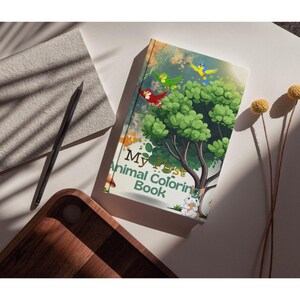 Op de afbeelding: Een kinder kleurboek "My First Animal Coloring Book" met een kleurrijke illustratie van een boom, vogels en een konijn. Het boek ligt op een wit oppervlak met een potlood, een notitieblok en een houten dienblad.