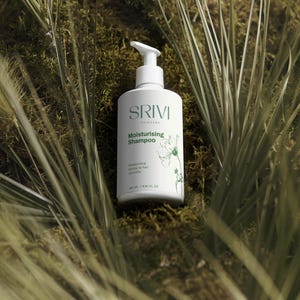 May include: A white SRIVI Moisturising Shampoo bottle with a pump dispenser, positioned amidst green foliage. The bottle displays the brand name and product information in a minimalist style. The bottle contains 260 ml of shampoo.