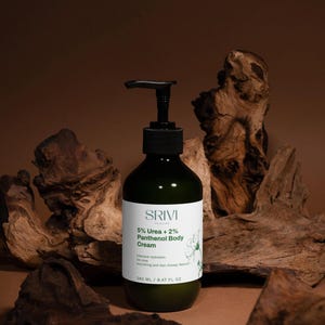 May include: A green body cream bottle with a black pump dispenser. The label reads "SRIVI 5% Urea + 2% Panthenol Body Cream." The bottle contains 9.47 fl oz. The background features wood pieces.