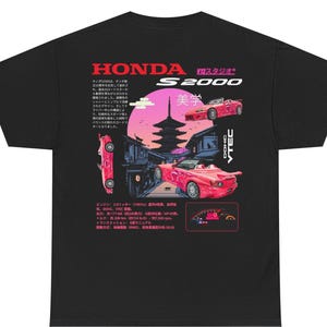 May include: Black t-shirt featuring a graphic design with the text "HONDA S2000" in red. The design includes illustrations of red cars, a pagoda, and Japanese text. The shirt has a classic crew neck and short sleeves.