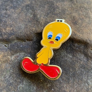 Pu&ograve; includere: Una spilla in smalto giallo raffigurante il personaggio dei cartoni animati Titti. La spilla ha un contorno dorato, occhi blu e scarpe rosse. Un oggetto da collezione.