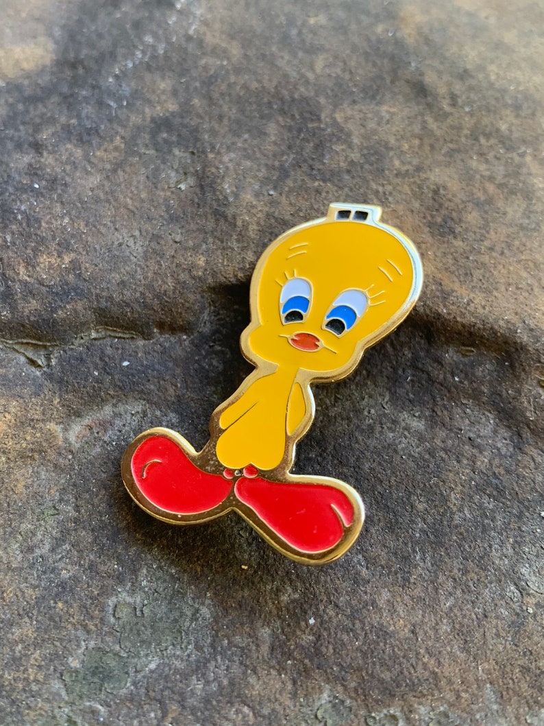 Pu&ograve; includere: Una spilla in smalto giallo raffigurante il personaggio dei cartoni animati Titti. La spilla ha un contorno dorato, occhi blu e scarpe rosse. Un oggetto da collezione.