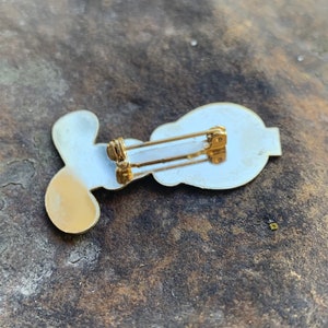 Pu&ograve; includere: Una spilla in stile vintage con un design bianco e oro. La spilla presenta una forma stilizzata con un retro dorato e una chiusura a spilla da balia. La spilla &egrave; probabilmente in metallo e ha una finitura lucida.