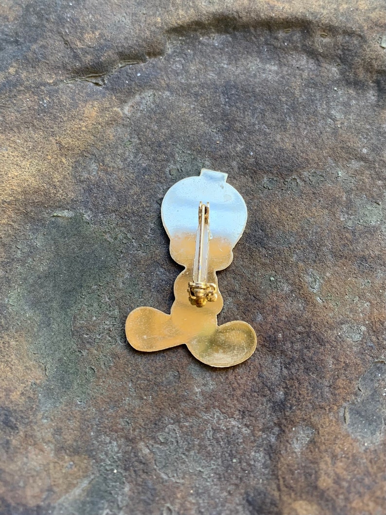 Pu&ograve; includere: Spilla in metallo color oro raffigurante un personaggio dei cartoni animati con una grande testa e piedi. La spilla ha una parte superiore color argento e un corpo color oro. La spilla &egrave; attaccata a una chiusura color oro.