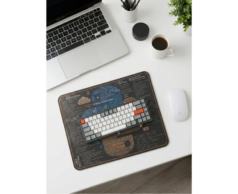 May include: A computer workspace with a laptop, a mechanical keyboard, and a mouse. A dark brown mousepad with white text and diagrams is under the keyboard. A cup of coffee and a small plant are on the white desk.