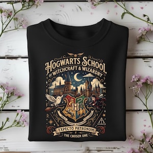 May include: A black sweatshirt featuring a graphic print of Hogwarts School of Witchcraft and Wizardry. The design includes a castle, a white owl, a crest with four animal emblems, the text "Expecto Patronum," and "The Chosen One."