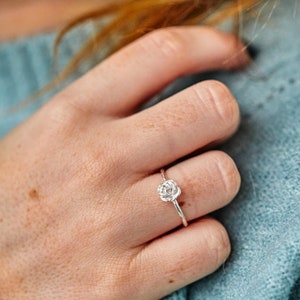 Puede incluir: Un anillo de plata con un delicado diseño de rosa. El anillo se lleva en el dedo de una persona.