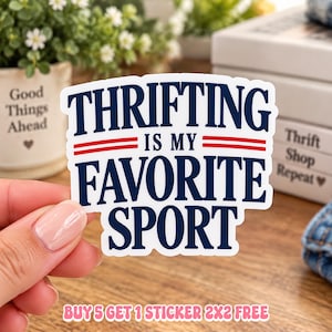 May include: A white die-cut sticker with dark blue text that reads THRIFTING IS MY FAVORITE SPORT, featuring two horizontal red lines between the words THRIFTING and IS MY, and two more red lines between IS MY and FAVORITE SPORT.